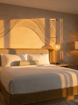 A cozy bedroom features a textured wall, soft lighting, and a neatly made bed, creating a warm and inviting ambiance.