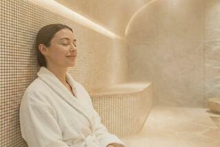 A woman in a white robe relaxes in a serene, steam-filled spa environment, exuding tranquility and calm.
