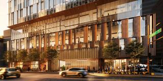 A modern building features a glass facade, wooden accents, and lush landscaping, bustling with people and vehicles in an urban setting.