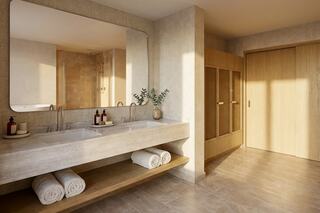 A modern bathroom features a sleek double vanity with large mirror, wood accents, neatly rolled towels, and a cozy, light-filled atmosphere.