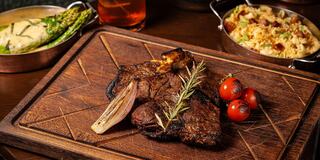 A succulent steak garnished with rosemary and cherry tomatoes, accompanied by asparagus and a creamy side dish, all on a wooden platter.