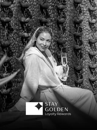 A woman in a bathrobe enjoys a drink while posing elegantly against a textured background, exuding a luxurious and relaxed vibe.