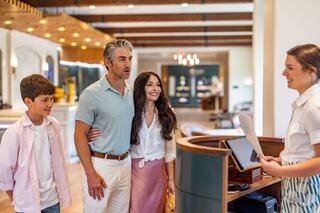 A family stands happily at a reception desk, engaging with a staff member, in a bright, welcoming environment.