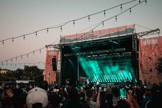 A lively outdoor concert scene with a large crowd, vibrant stage lights, and a sunset backdrop, creating an energetic festival atmosphere.