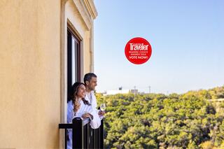 A multi-story hotel nestled among greenery, featuring light-colored architecture and numerous balconies, with a scenic backdrop and an award banner.
