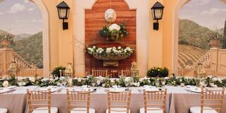 A beautifully arranged long table adorned with flowers and greenery, set against a rustic backdrop of rolling hills and elegant sconces.
