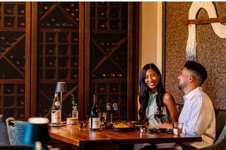 A couple enjoys a romantic dinner, smiling at each other, surrounded by elegant wine storage and a cozy, intimate atmosphere.