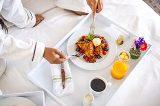 A cozy breakfast scene featuring French toast topped with ice cream and berries, accompanied by coffee, juice, and fresh flowers on a tray.