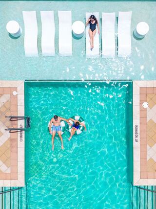An aerial view of a vibrant pool scene, featuring lounge chairs and two people enjoying the water, radiating relaxation and leisure.