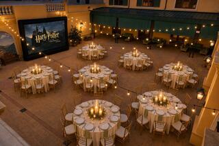 An elegant outdoor setting features beautifully arranged tables with glowing candles, highlighted by a large screen showing "Harry Potter."